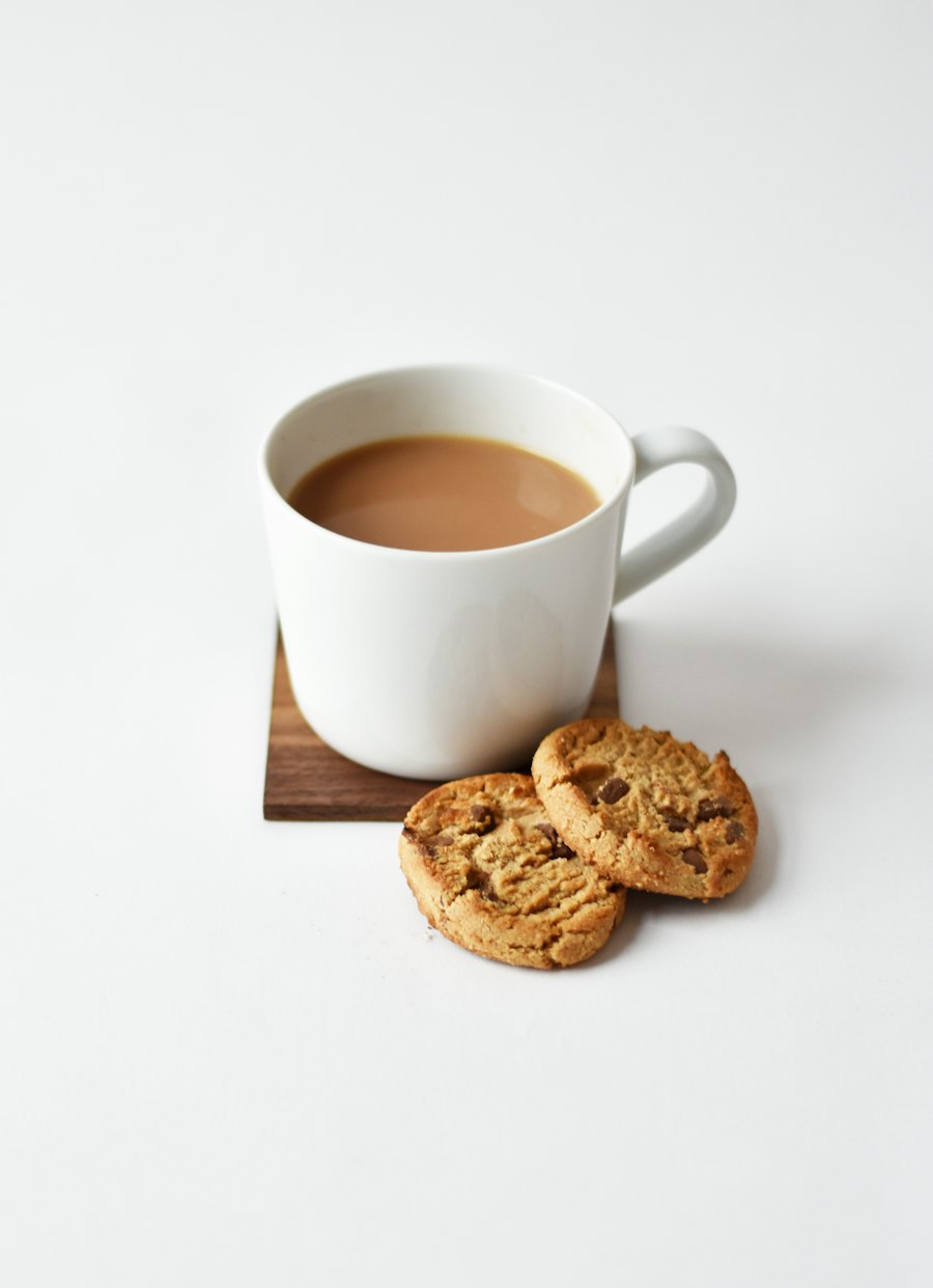 White ceramic mug of tea on a wooden coaster next to cookies, the blank we print on